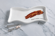 White wavy dish with a strip of bacon and 'What's shakin' bacon' text on a marble surface.