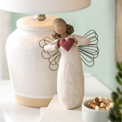 Decorative angel figurine with a heart on a table with a lamp in the background