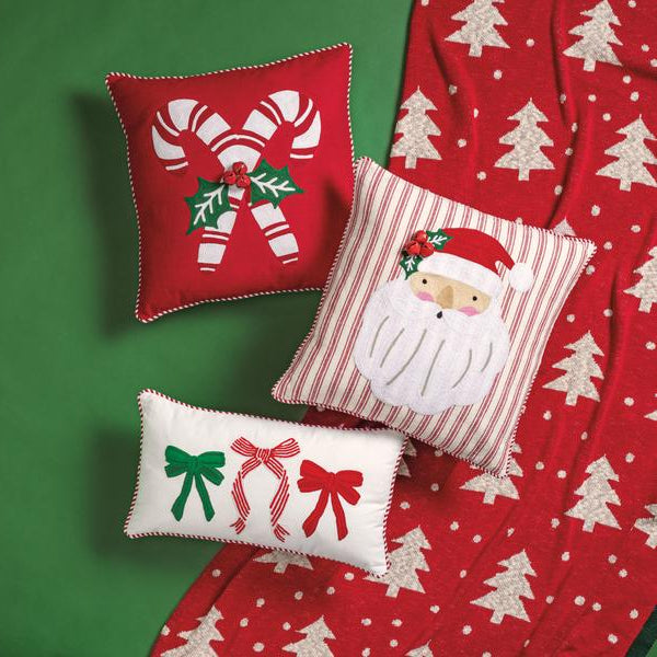 Three Christmas-themed decorative pillows on a red fabric background with tree patterns.