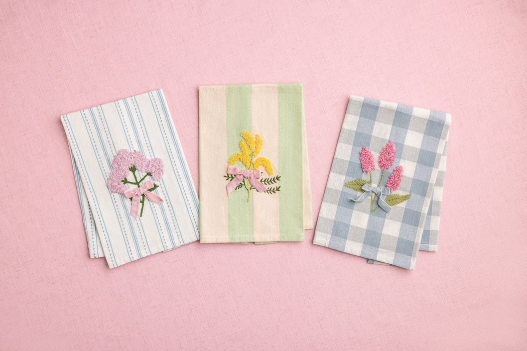 Three embroidered napkins with floral designs on a pink background