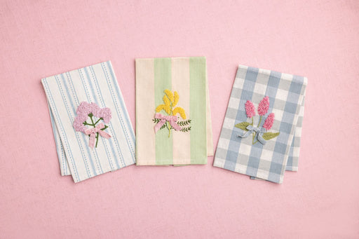 Three embroidered napkins with floral designs on a pink background