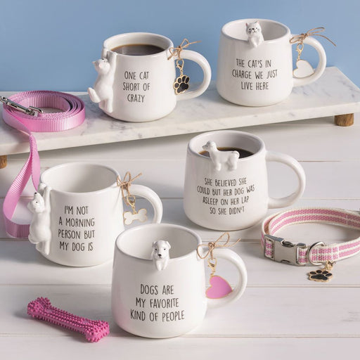 Set of ceramic mugs with dog-themed sayings on a white surface with pet accessories.