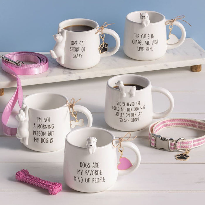 Set of ceramic mugs with dog-themed sayings on a white surface with pet accessories.