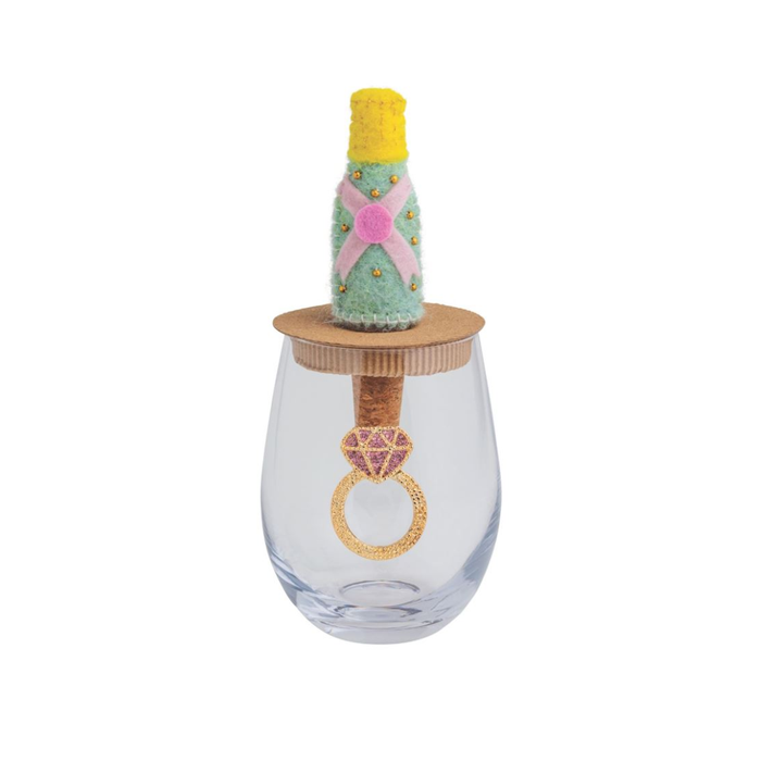 Decorative wine glass with a cork stopper and small bottle on top, featuring a pink gemstone ring design.