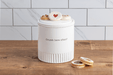 White cookie jar with text on a wooden surface and tiled wall background