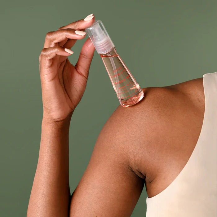 Person applying a clear bottle with pink liquid to their shoulder against a green background