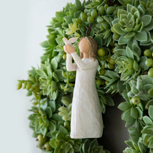 Decorative wreath with a figurine of a woman holding a heart, set against a white background.