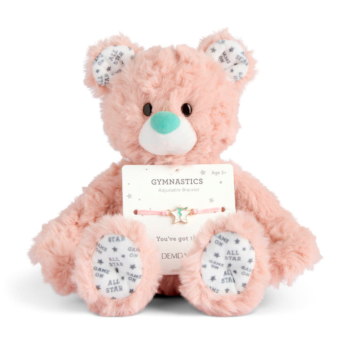 Pink teddy bear with a gymnastics-themed bracelet and card on a white background