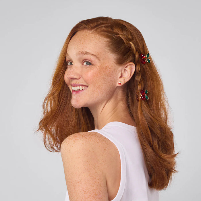 Woman with red hair styled in a ponytail with decorative hair clips on a light gray background