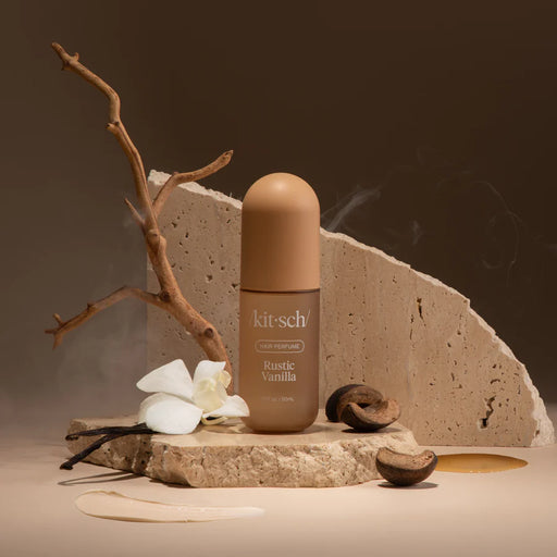 Kitsch Rustic Vanilla perfume bottle on a stone surface with vanilla beans and flowers.