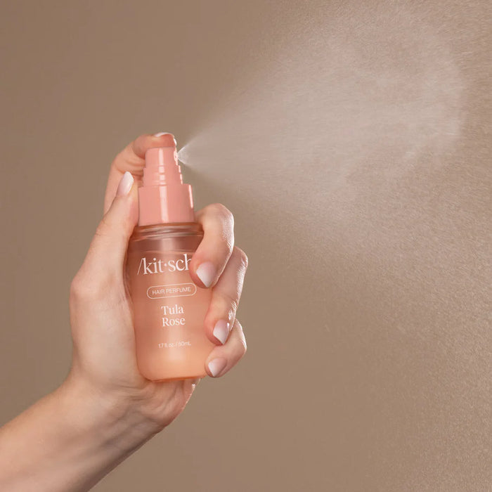 Hand holding a pink spray bottle labeled 'Akitsch' with mist being released against a beige background.
