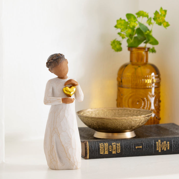 Decorative figurine holding a heart, placed on books with a vase and plant in the background.