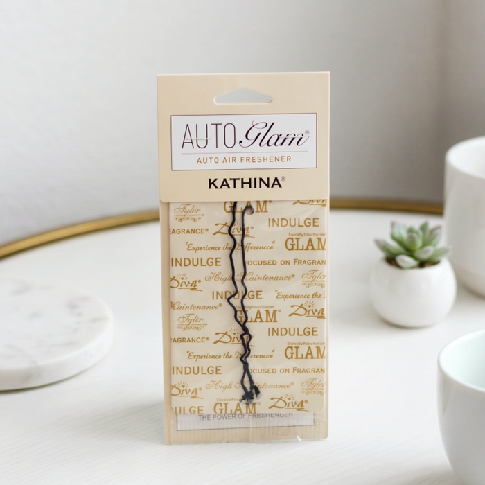 Kathina Auto Glam air freshener packaging on a white surface with decorative elements.