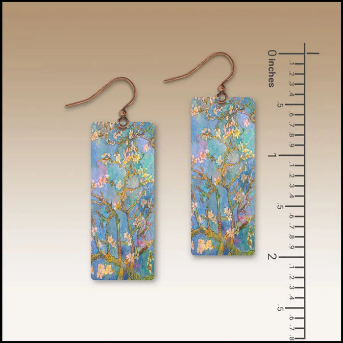 Pair of rectangular earrings with floral design next to a ruler for scale on a beige background