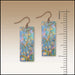 Pair of rectangular earrings with floral design next to a ruler for scale on a beige background