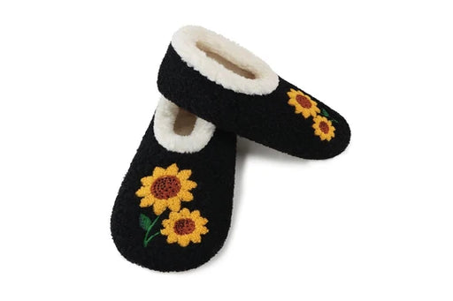 A pair of black fuzzy slipper shoes with white sherpa lining and embroidered yellow sunflowers on a white background.