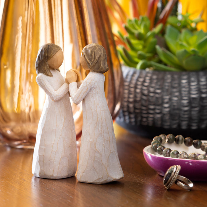 Two standing, separate figures in cream dresses facing each other, with hands that interlock together. Hands of one figure fit into hands of other figure