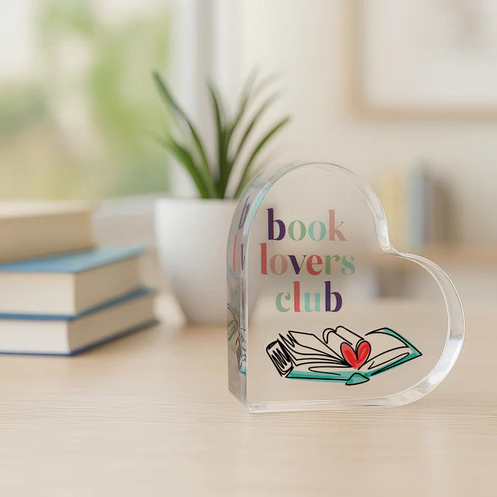 Heart-shaped glass object with 'book lovers club' text and book illustration on a blurred background
