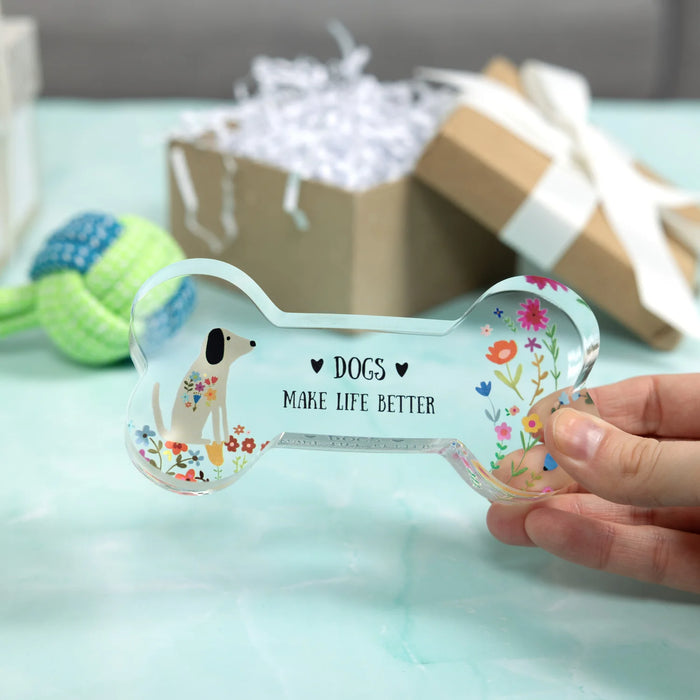 Clear bone-shaped pet tag with floral design and text held by a hand on a light blue surface.