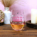 Stemless wine glass with 'LET'S GO GIRLS' text on a wooden table with decorative items.