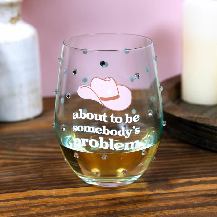 Glass with a cowboy hat design and text 'about to be somebody's problem' on a wooden surface.
