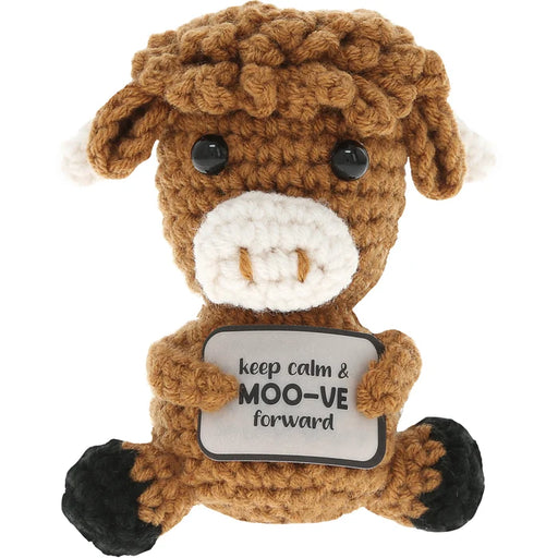 A brown crocheted plush cow toy holding a sign that reads 'keep calm & MOO-VE forward'. The toy has a white snout and ears, black eyes, black hooves, and is photographed against a solid white background.