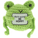 Green knitted frog toy with a sign saying 'don't worry BE HOPPY' on a white background