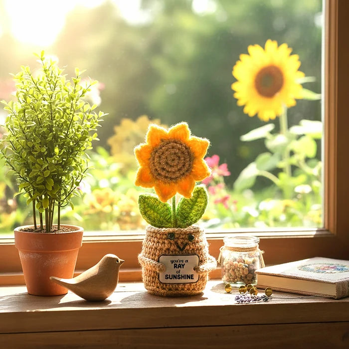 Sunflower-themed knitted decoration on a windowsill with plants and a book in the background.