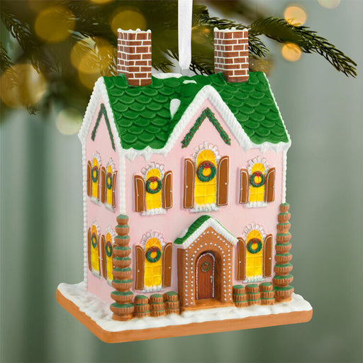 Decorative gingerbread house ornament with green roof and pink walls, hanging on a tree.