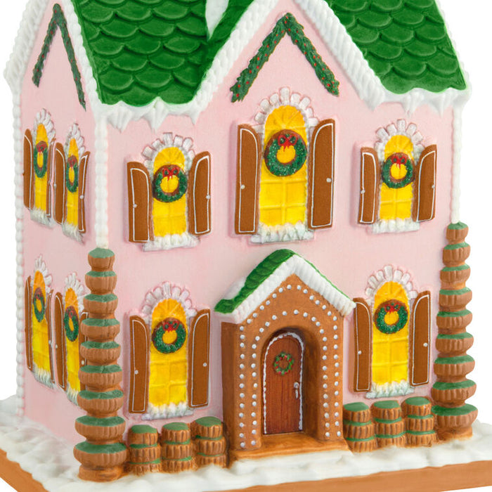 Decorative gingerbread house with pink walls, green roof, and yellow windows.