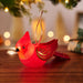 Red cardinal-shaped ornament on a wooden surface with blurred lights in the background