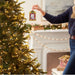 Person decorating a Christmas tree with an ornament in a festive living room.