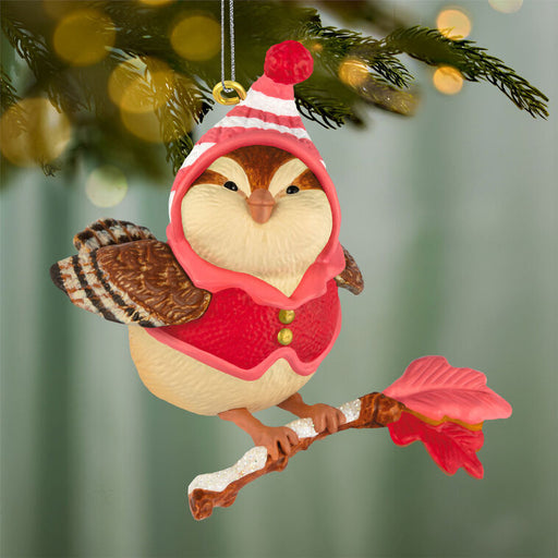 Decorative bird ornament in a red outfit on a branch hanging on a Christmas tree.