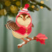 Decorative bird ornament in a red outfit on a branch hanging on a Christmas tree.