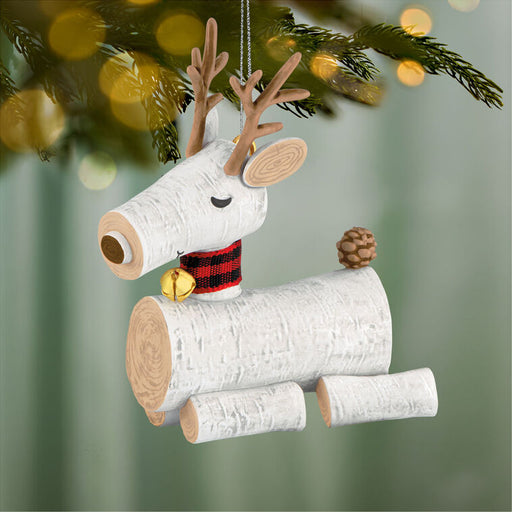 Decorative reindeer ornament made of logs with a plaid scarf and pine cone, hanging on a Christmas tree.