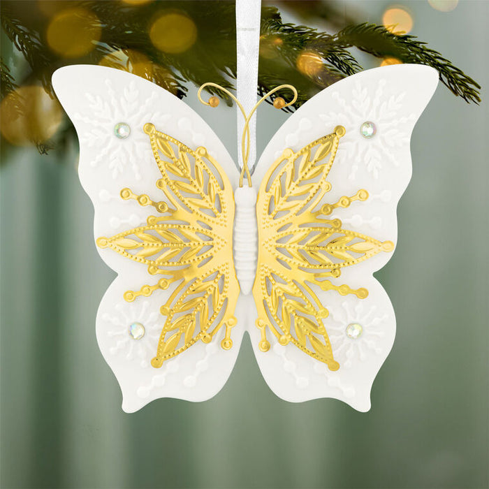 Decorative butterfly ornament with gold and white design on a blurred Christmas tree background