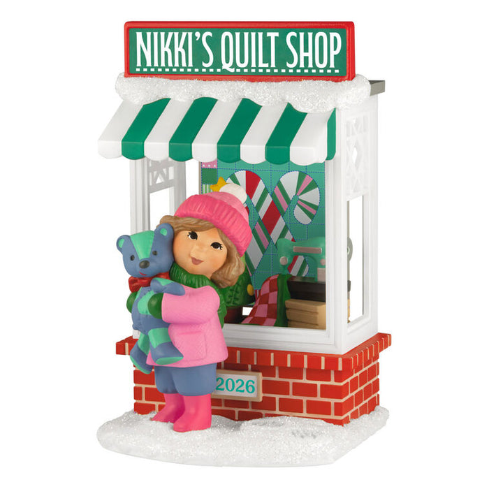 Ornament of a girl holding a teddy bear in front of Nikki's Quilt Shop