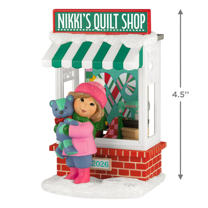Ornament of a girl with a teddy bear in front of 'Nikki's Quilt Shop' with dimensions indicated.