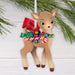 Decorative reindeer ornament with a candy cane, bells, and a 'Merry Christmas' tag, hanging against a white background with greenery.