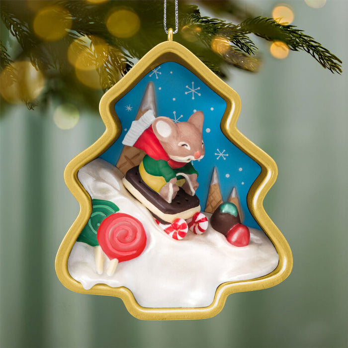 Christmas ornament with a mouse in a tree-shaped frame against a blurred Christmas tree background.