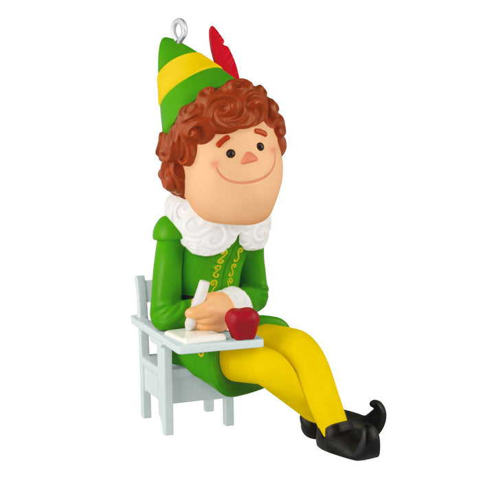 Christmas ornament of an elf sitting on a chair with a book and apple, wearing a green outfit with a green and yellow hat.