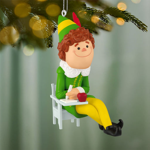 Elf ornament sitting on a chair with a green and yellow hat, green outfit, and yellow pants, hanging from a Christmas tree.