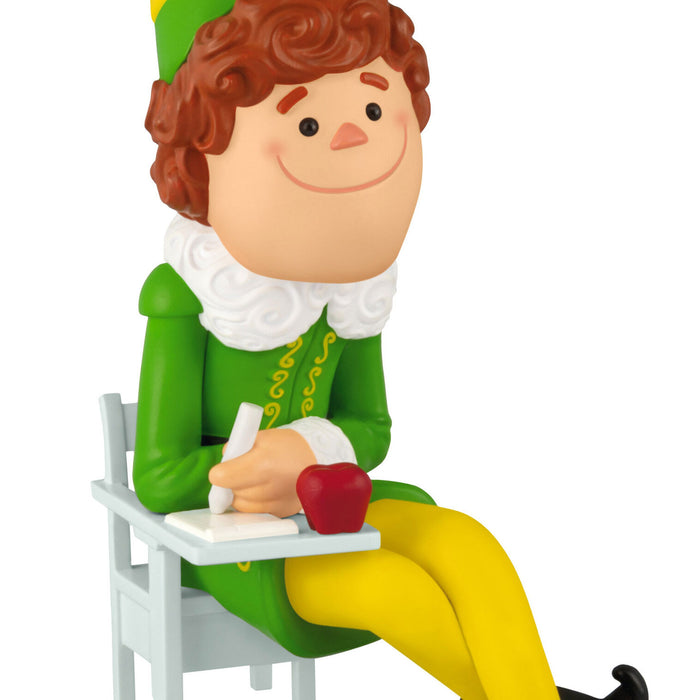 Figurine of an elf character in a green outfit with a red apple, sitting on a white chair.