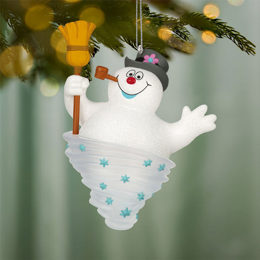 Christmas ornament of a snowman with a broom and top hat hanging on a tree.