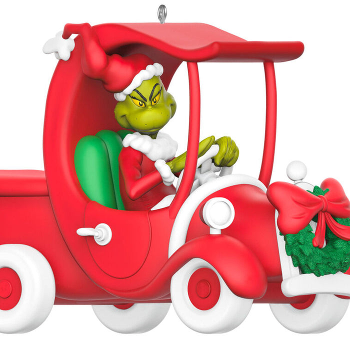 Decorative ornament of the Grinch driving a red car with a wreath on a white background