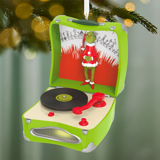 Decorative ornament resembling a record player with the Grinch in a Santa outfit, hanging from a tree.