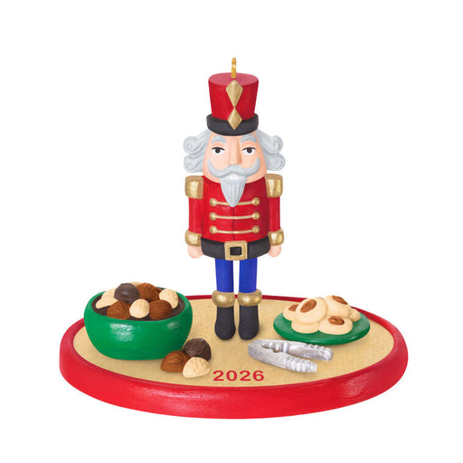 Christmas nutcracker figurine with a red outfit and white beard, standing on a platform with cookies and a bowl of nuts, on a white background.