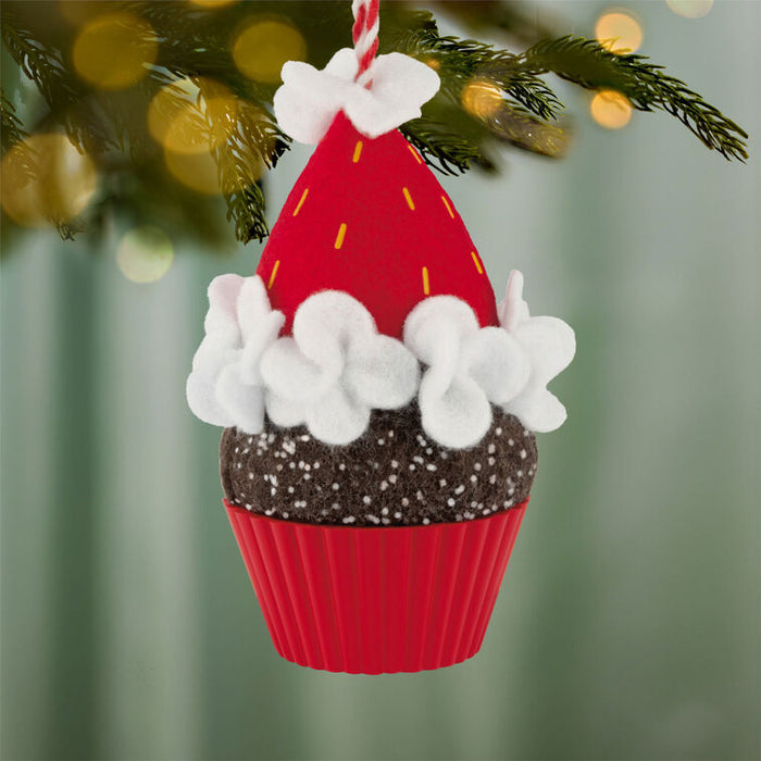 Decorative Christmas ornament shaped like a cupcake with a red and white frosting, hanging on a tree.