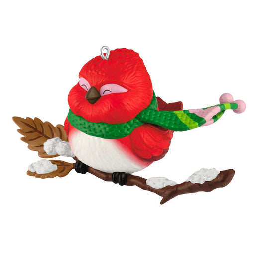 Red bird ornament with green scarf on a branch against a white background