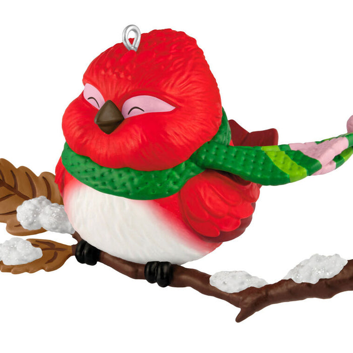 Decorative red bird ornament with a green scarf on a branch against a white background